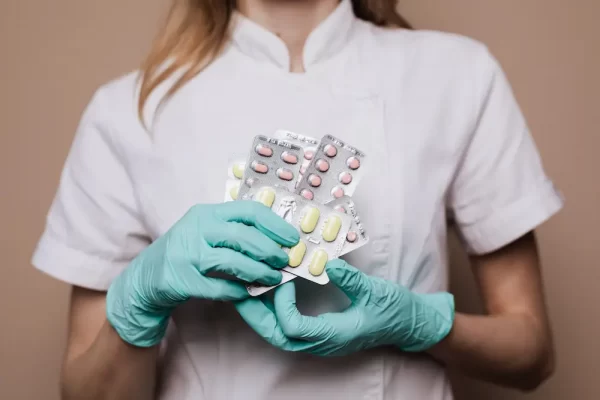 Profissional de saúde com luvas segurando medicamentos, destacando a biossegurança em laboratório.