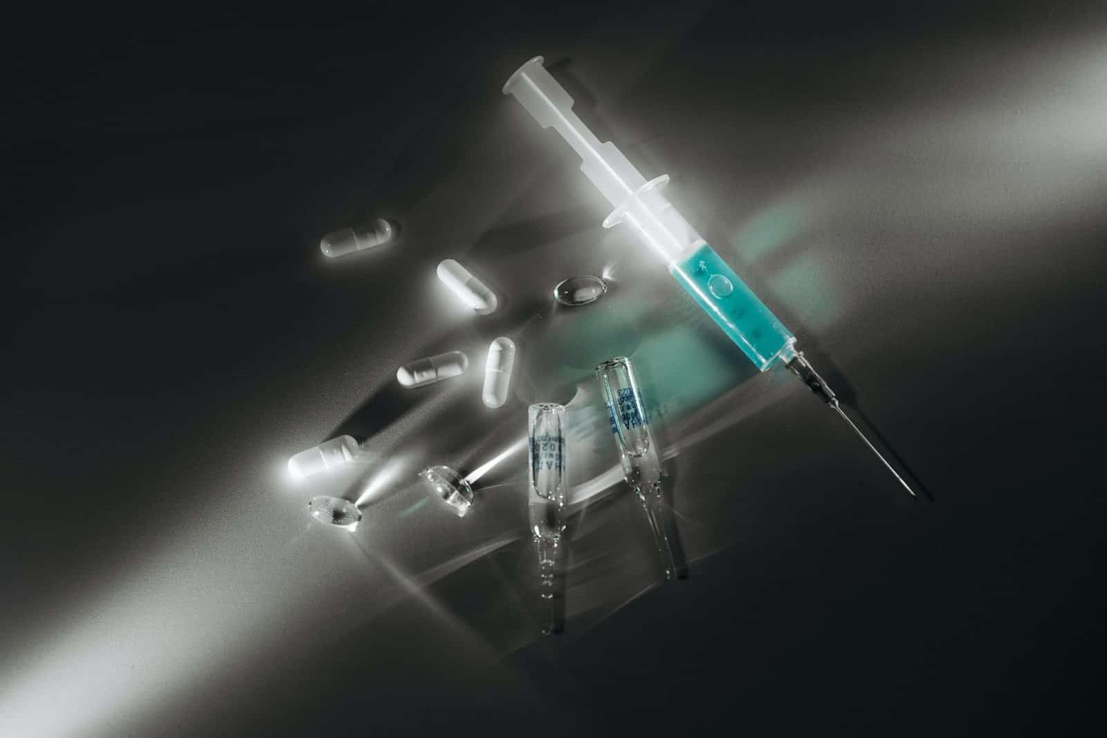 Seringa, frascos de medicamento e comprimidos espalhados por uma superfície plana