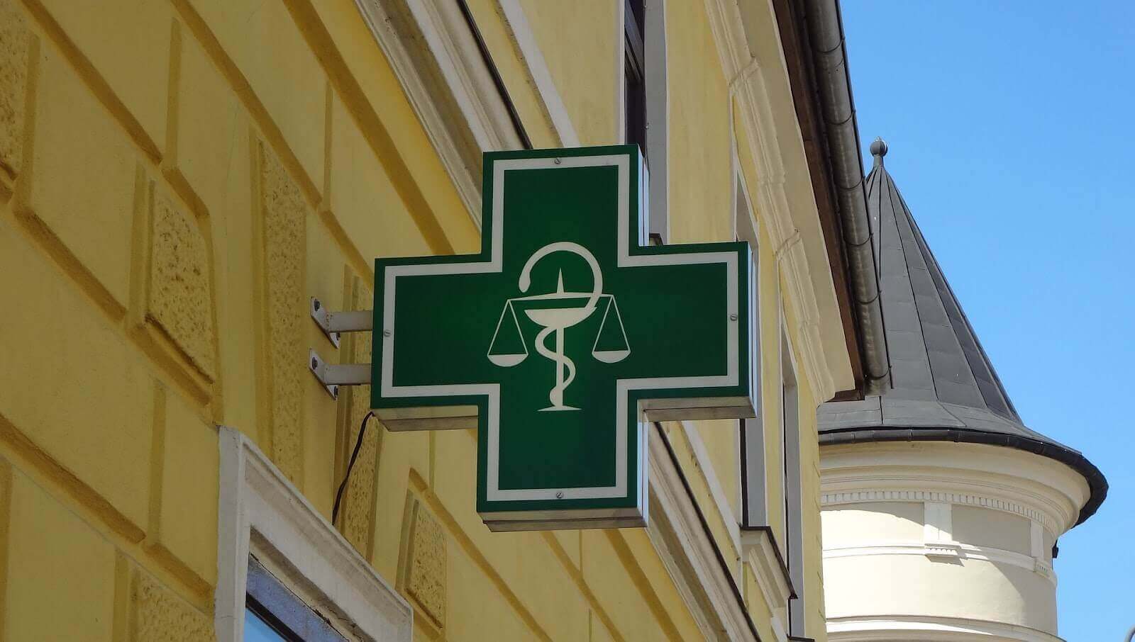 Placa verde em formato de cruz com logo da farmácia