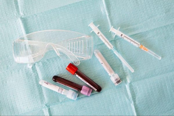Frascos de coleta de sangue, seringas e óculos de proteção sob uma superfície plana